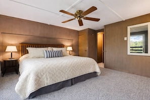 A bedroom with a bed, two bedside tables with lamps, a ceiling fan, a wardrobe, and a window with a view.