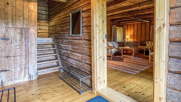 L’intérieur d’une cabane en rondins, avec un escalier en bois, un étagère en métal et un coin repas comprenant une table et des chaises.