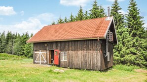 Une cabane rustique en bois, avec un toit recouvert de tuiles rouges, une cheminée et une structure en forme de croix à l’avant.