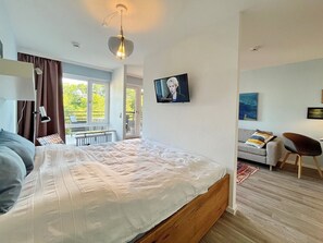 Quarto moderno com cama grande, televisão, sofá e varanda com vista.