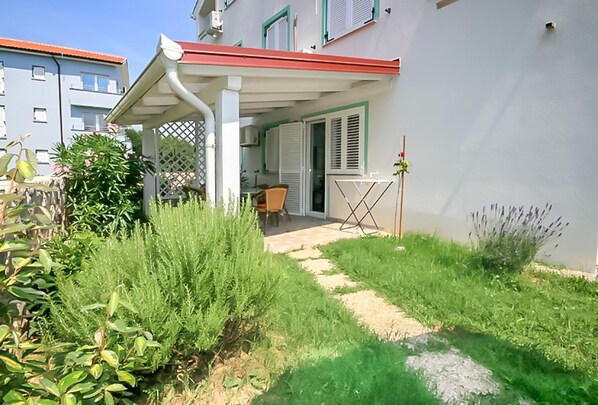 A residential property with a covered patio, a small outdoor seating area, and a garden with various plants. - Flat with air conditioning, WiFi, BBQ and garden (Baska)