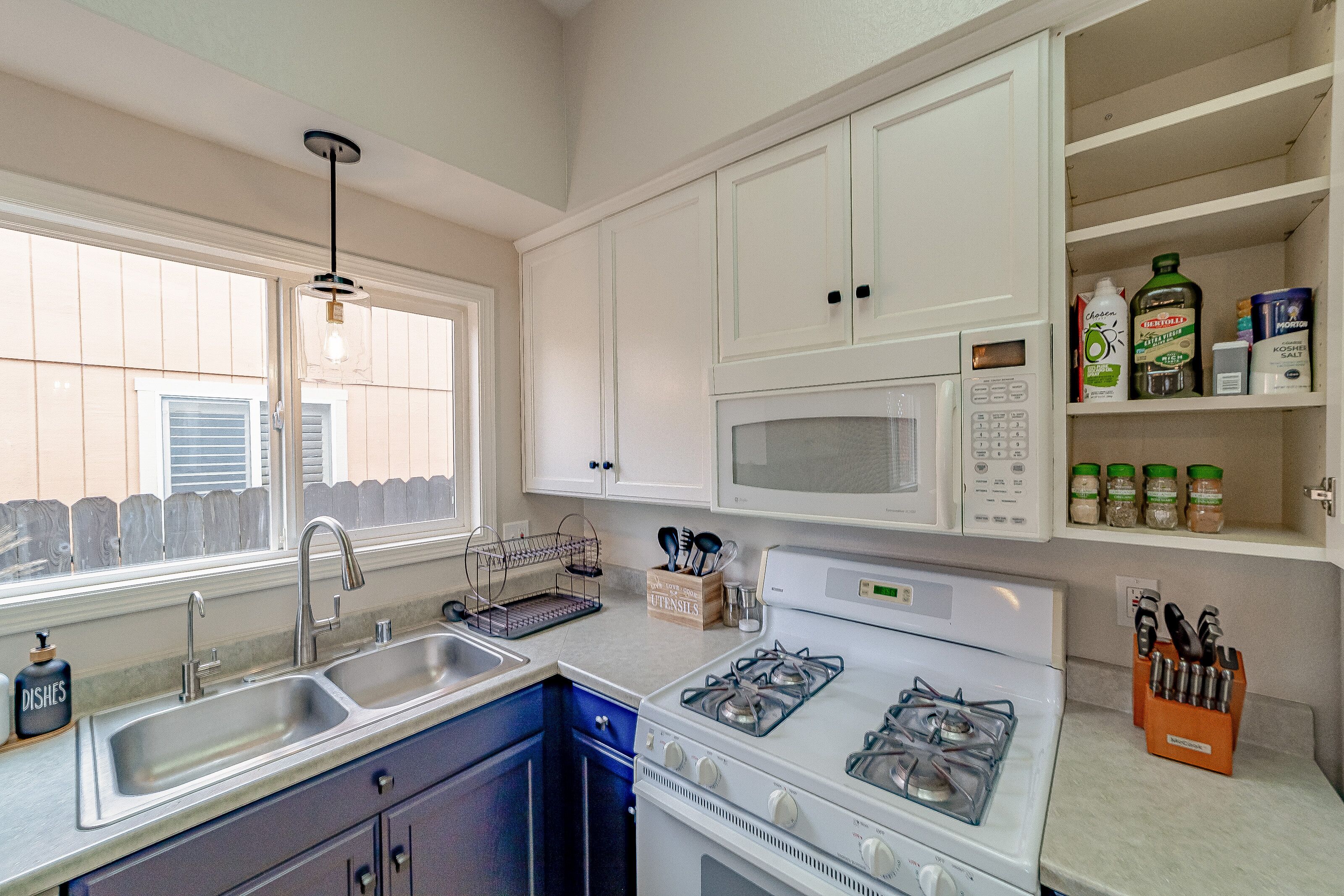 A kitchen with a double sink, stove, microwave, and cabinets.