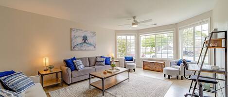 A spacious living room with a gray sofa, a wooden coffee table, and a white armchair.