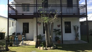 Una casa de dos pisos con un balcón, plantas en macetas y un pequeño espacio exterior con mesas y sillas.