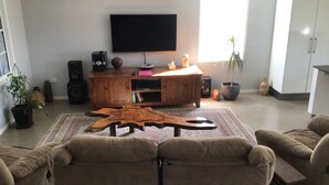 Una sala de estar con un mueble bajo de madera para el equipo de entretenimiento, un televisor de pantalla plana y una mesa de centro. Hay dos sofás y una planta en maceta.