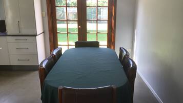 Uma área de refeições com mesa posta para quatro pessoas, janela com vista para um jardim e uma cozinha compacta com armários e bancada.