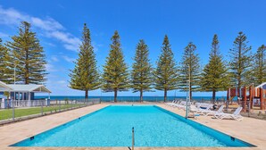 A rectangular swimming pool with a clear blue water, surrounded by a tiled deck. There are lounge chairs and a fence along the pool's edge. - RAC Esperance Holiday Park (Castletown)