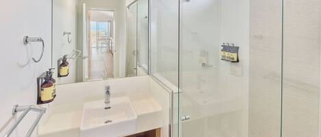 Une salle de bain moderne avec une douche à parois de verre, un lavabo blanc et un miroir.