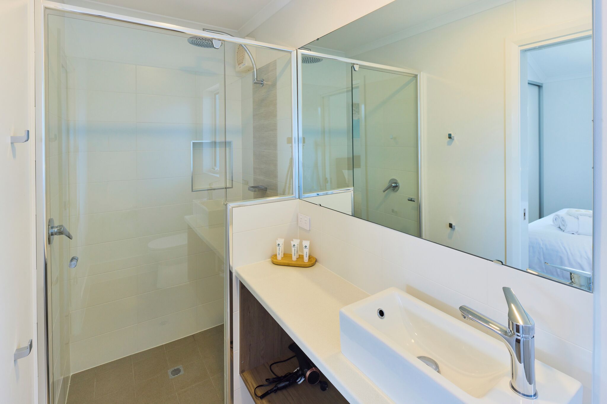 Un baño moderno con ducha envuelta en cristal, un lavamanos blanco con grifo cromado y un espejo sobre él.
