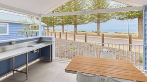 A covered outdoor area with a wooden table and chairs, a stainless steel counter, and a view of the beach and trees. - RAC Esperance Holiday Park (Castletown)