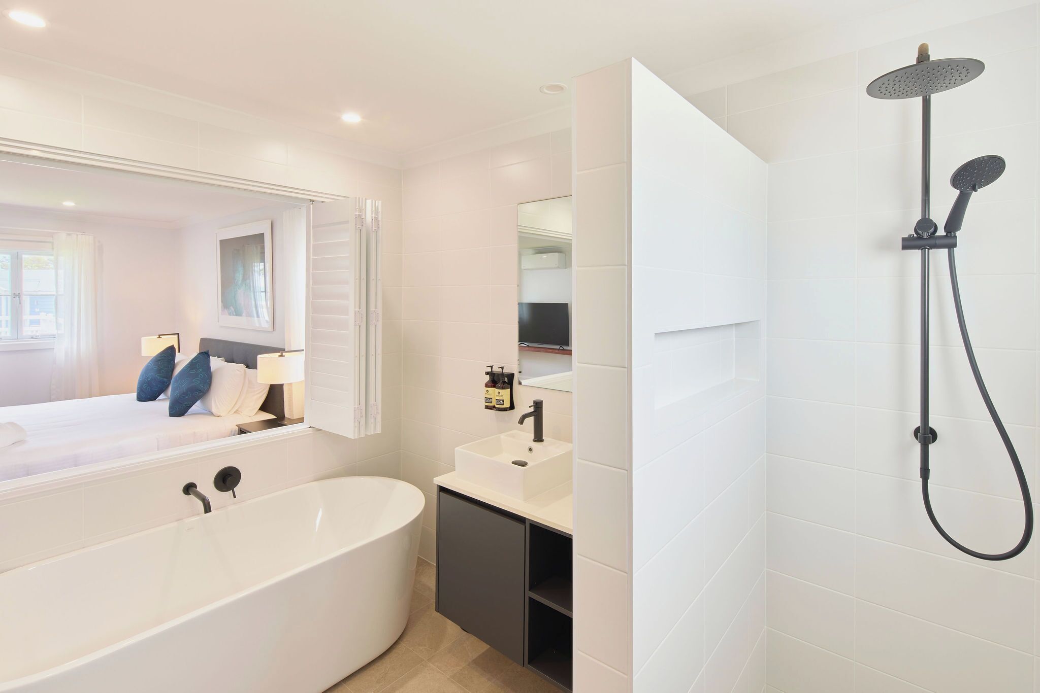 Un baño moderno con una bañera independiente, un cabezal de ducha empotrado y un espejo grande sobre el lavamanos.