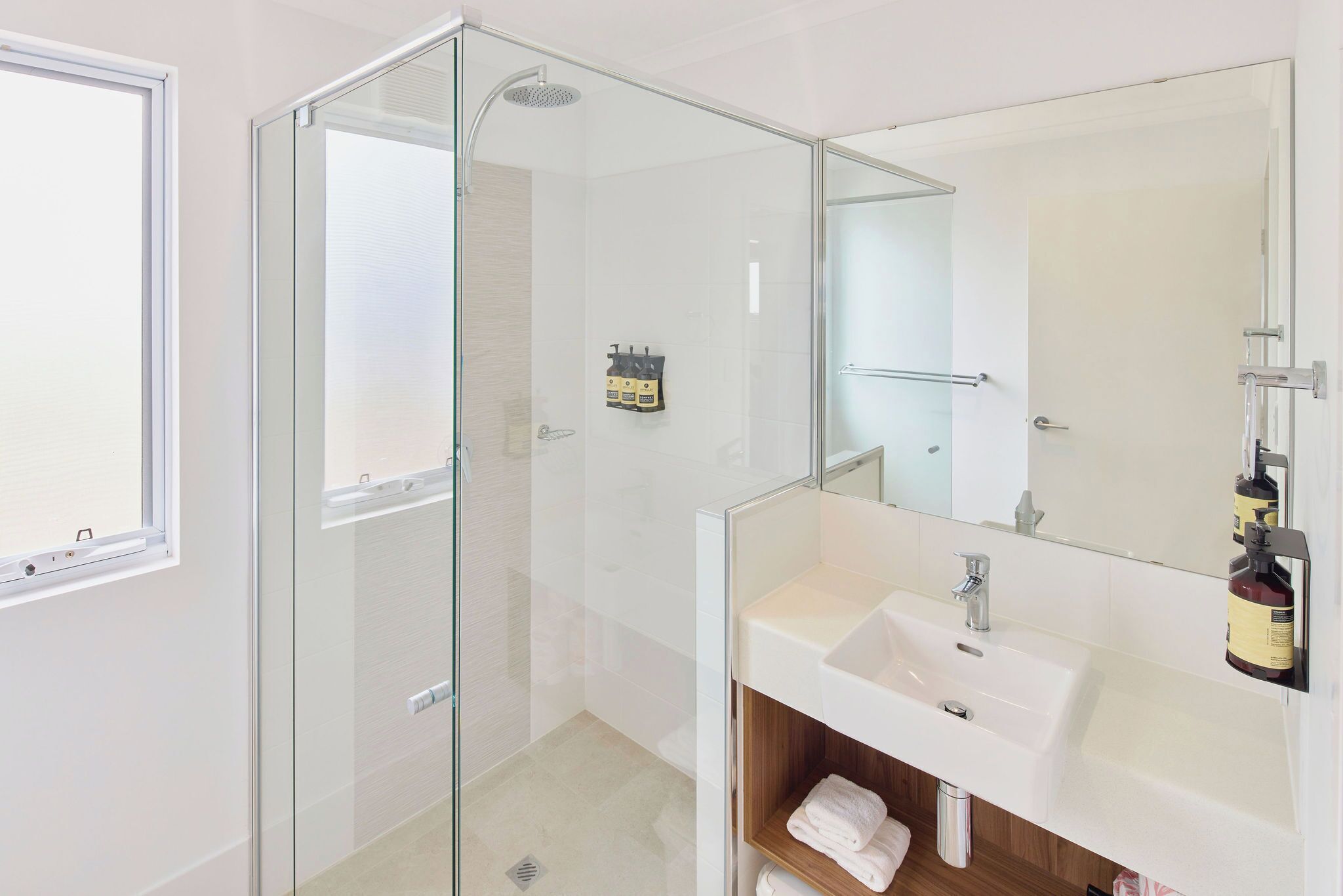 Un baño moderno con ducha acristalada, lavabo blanco y un espejo grande.