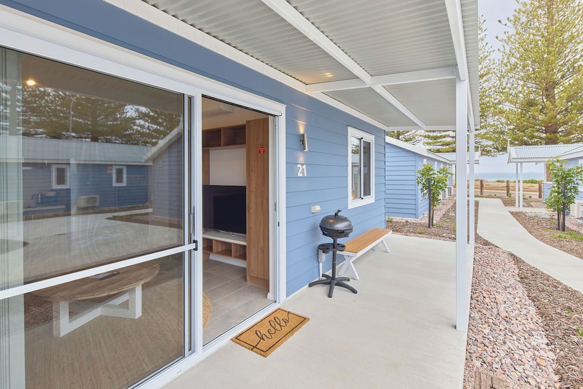 A modern building with a sliding glass door entrance, a barbecue grill outside, and a bench.