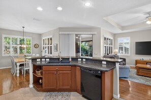 A modern kitchen with a built-in dishwasher, a dining area with a wooden table and chairs, and a living room with a sofa and a flat-screen TV. - GOLF paradise The Villages 3 bed 2 bath FREE golf cart near Lake Sumter Landing (The Villages)