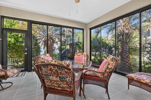 A sunlit room with wicker furniture, large windows, and a view of tropical vegetation. - GOLF paradise The Villages 3 bed 2 bath FREE golf cart near Lake Sumter Landing (The Villages)
