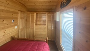 Una camera in legno con un letto, una ventola a soffitto, una finestra con persiane e un riscaldatore a parete.