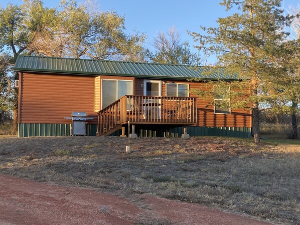 A cabin with a deck, a grill, and a window.