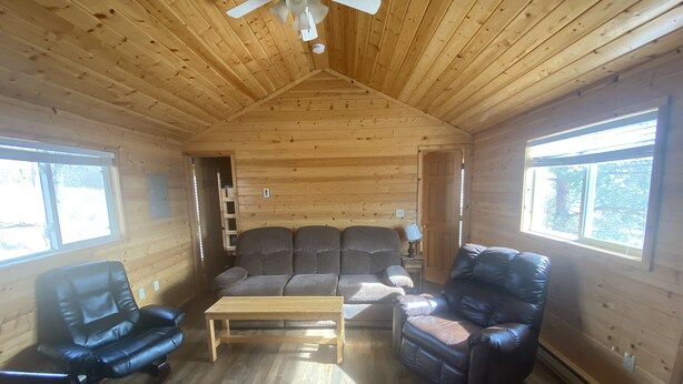 Interno di una baita in legno con una ventola a soffitto, un divano, due poltrone in pelle e un tavolino in legno.