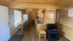 Interno di una baita in legno con angolo cottura, tavolo da pranzo e televisore.