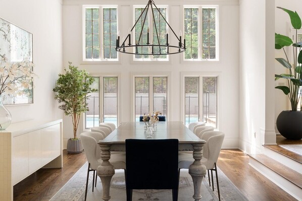 Enjoy meals in this elegant dining room with a large table and six chairs, a high ceiling, and a view of the outdoors.