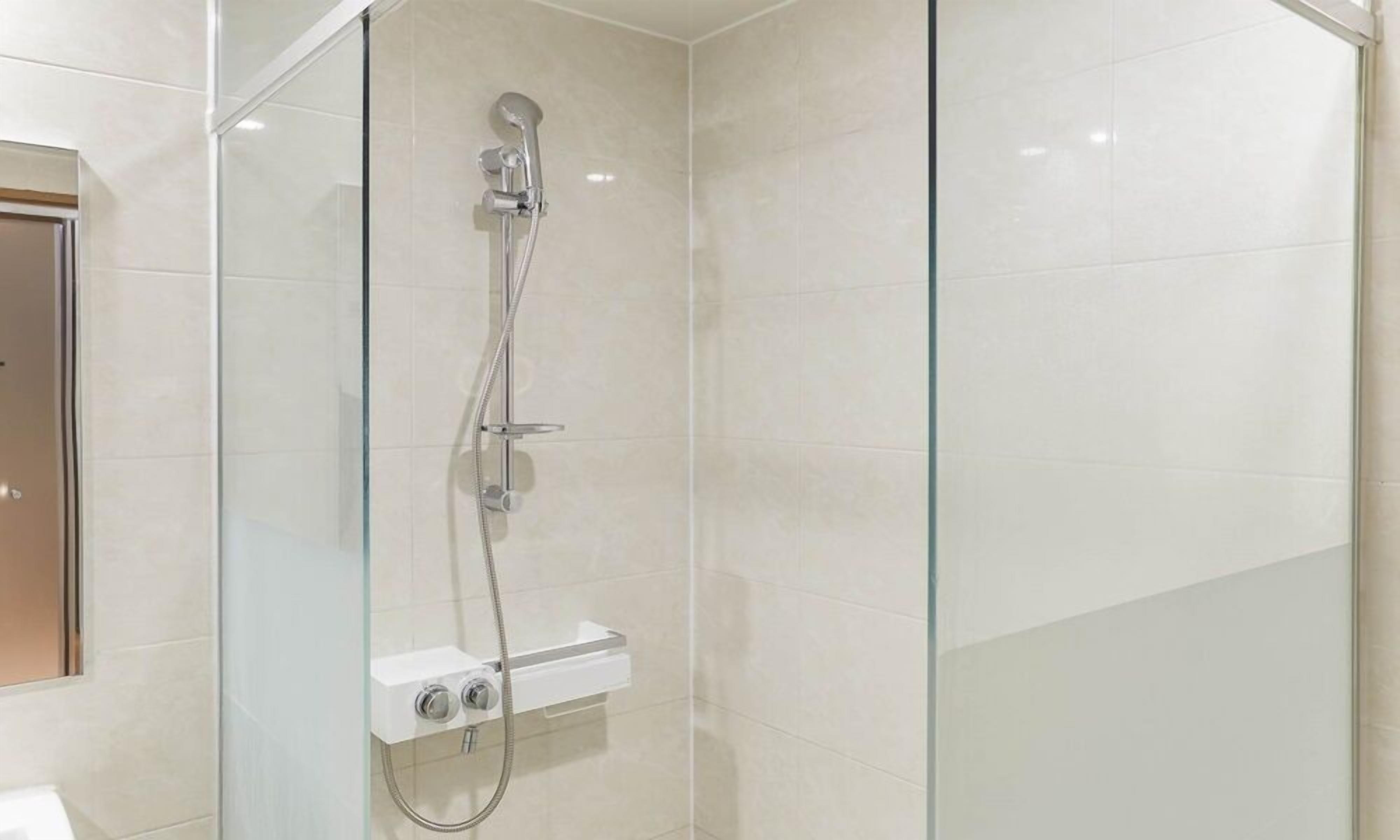Une douche moderne dotée d’un pare-douche en verre, d’un pommeau de douche à main et d’un panneau de commande.