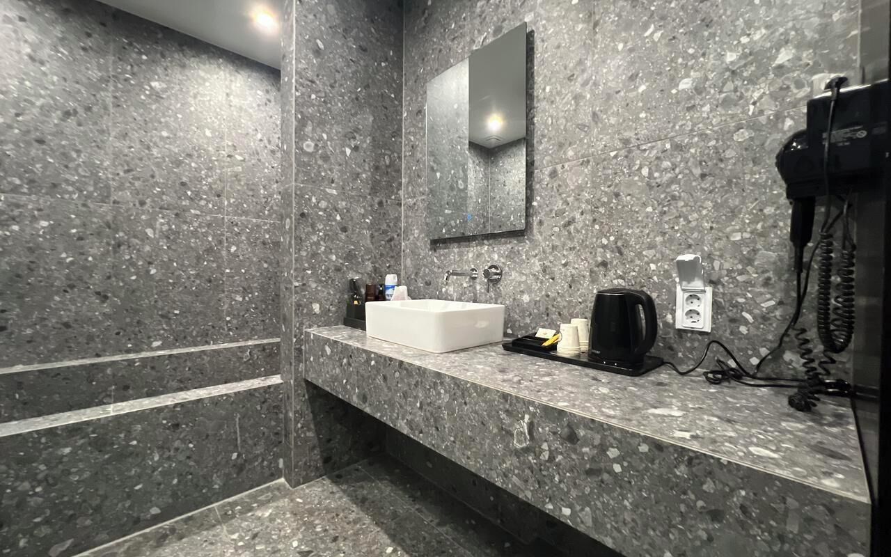 A modern bathroom with a granite countertop, a white sink, a mirror, and a hairdryer on the wall.
