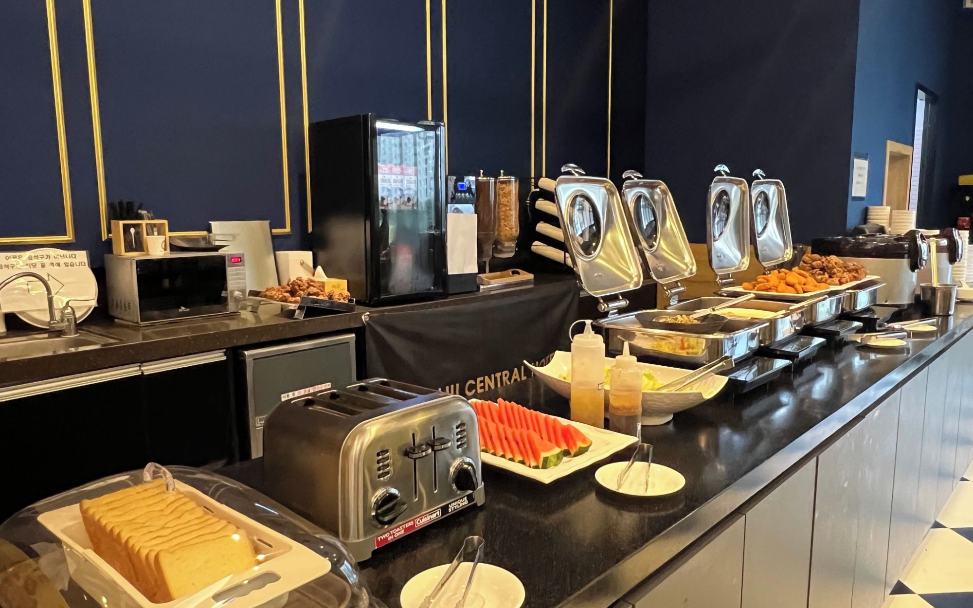 A buffet counter with various food items, a toaster, and a refrigerator.