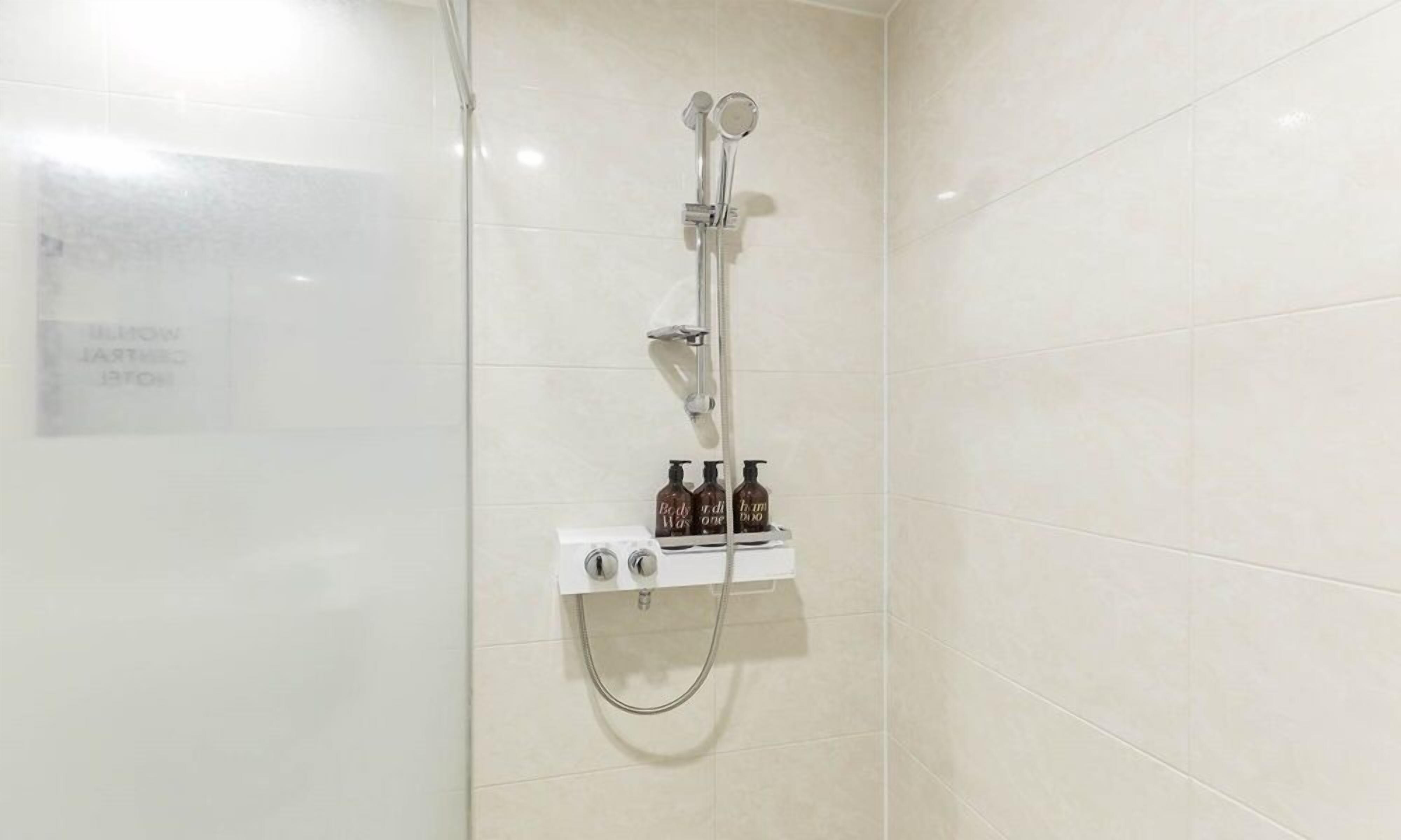 Ducha con cabezal de ducha de mano y grifo empotrado en la pared, panel de control y dos botellas de gel de baño.