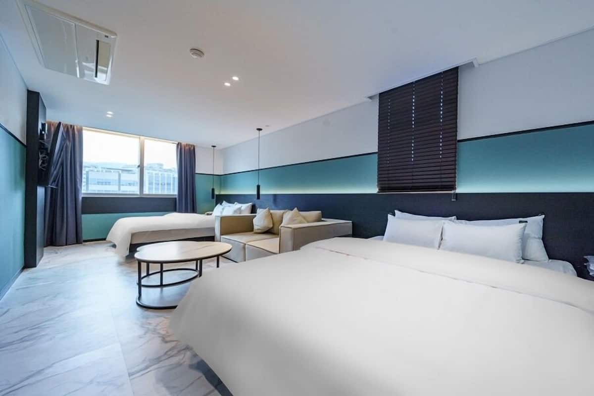 Een moderne hotelkamer met twee bedden, een bank, een tafeltje en uitzicht op de stad.