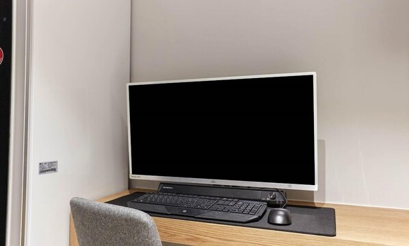 Un espacio de trabajo moderno con un monitor de pantalla plana grande, un teclado mecánico y un ratón sobre un escritorio de madera.