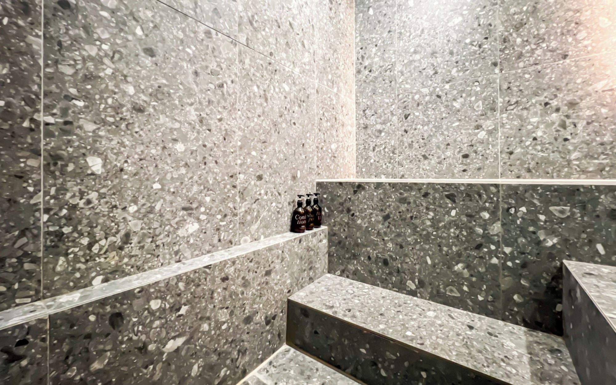 A modern bathroom with terrazzo flooring and a built-in bench.