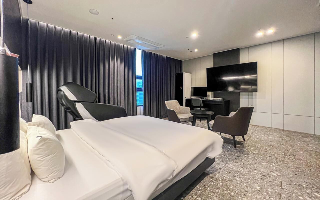 A modern hotel room with a large bed, a desk, a chair, and a flat-screen TV.