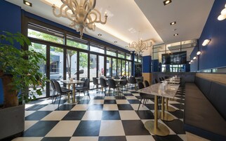 Un restaurante con suelo de cuadros, sillas blancas y negras y una larga barra con encimera de mármol.