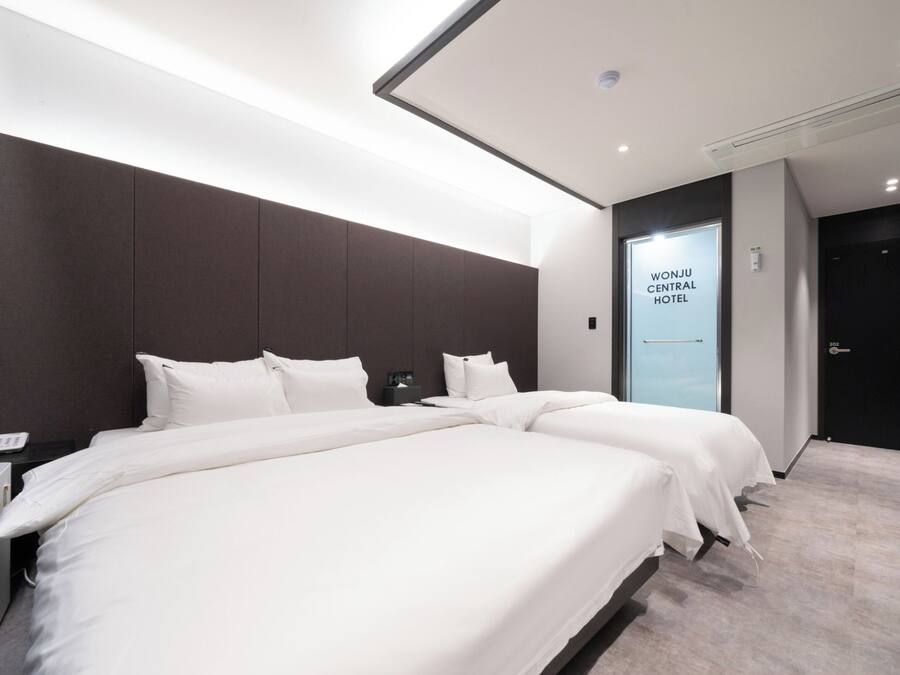 A hotel room with a large bed, a bedside phone, and a wall-mounted air conditioning unit.