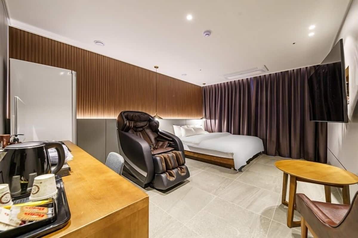 Een hotelkamer met een massagestoel, een bed, een bureau met een koffiezetapparaat en een televisie.