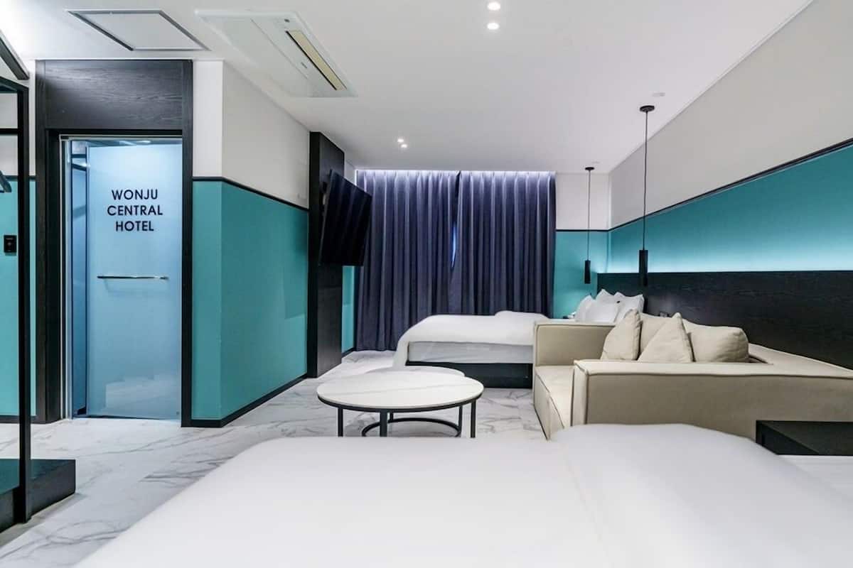 Een moderne hotelkamer met een groot bed, een bank, een klein rond tafeltje en een deur met de tekst 'WONJU CENTRAL HOTEL'.