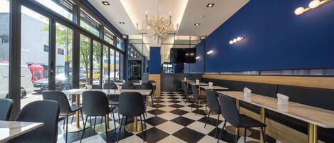 A modern restaurant interior with checkered flooring, black and white chairs, and a blue accent wall.