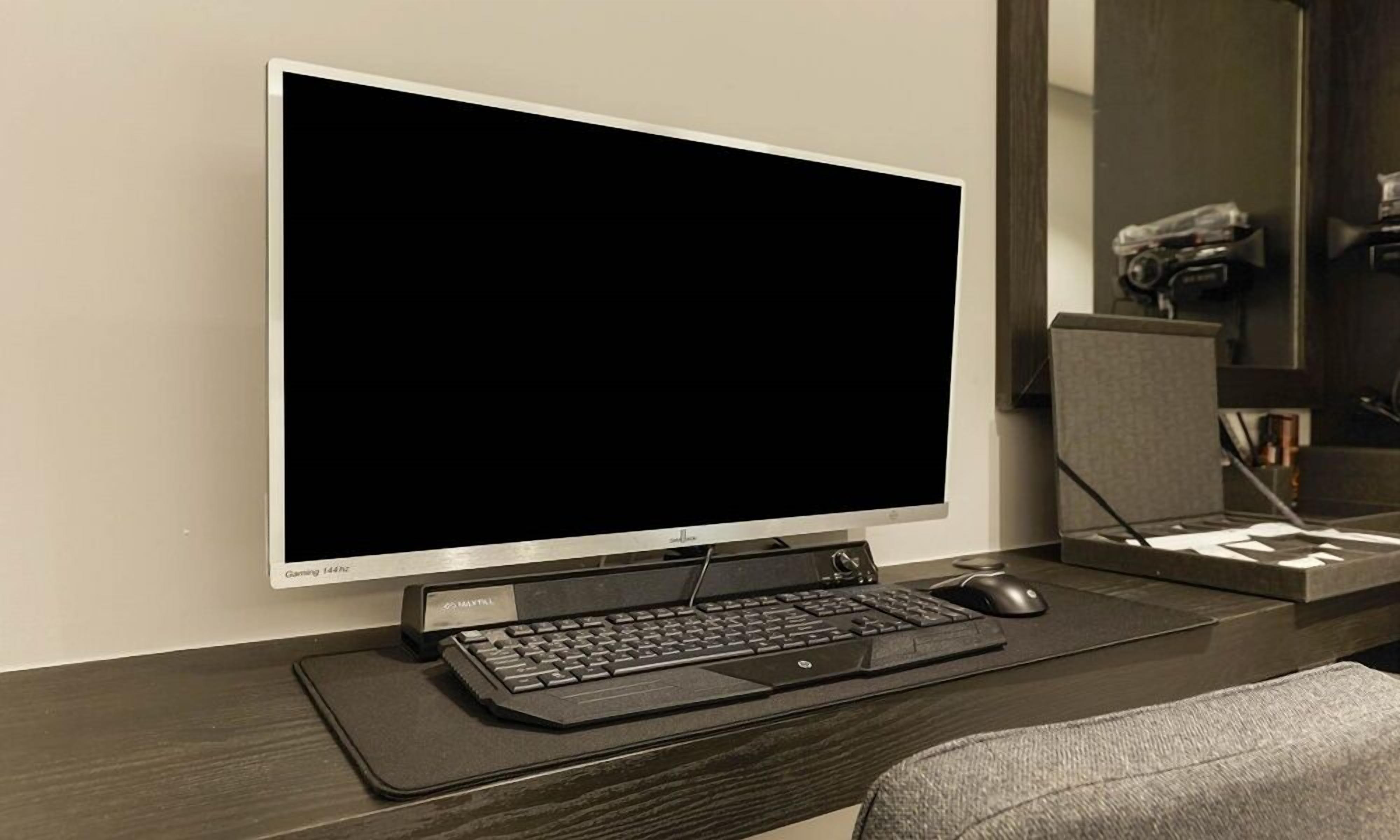 A modern office setup with a large monitor, a keyboard, and a mouse on a dark desk.