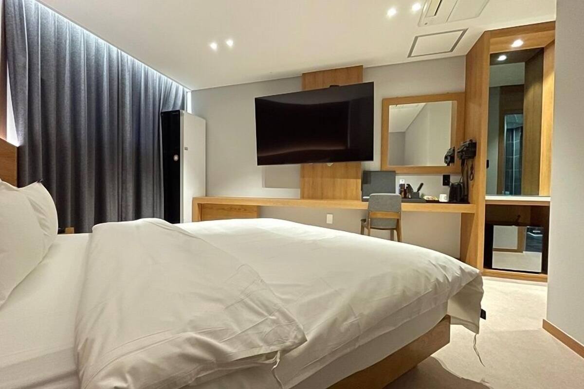 Een moderne hotelkamer met een groot bed, een bureau met een computer, een flatscreen televisie en een spiegel.