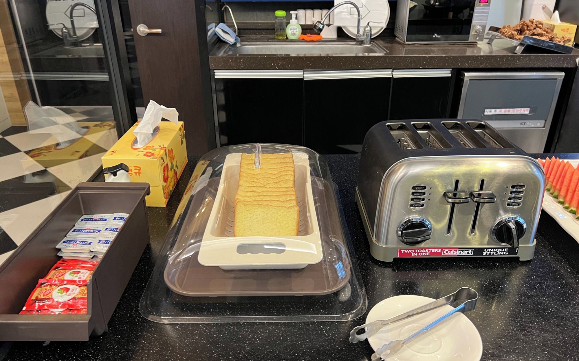Un plan de travail de cuisine avec deux grille-pain, un four à griller, une assiette de pain et une boîte de portions individuelles de beurre.