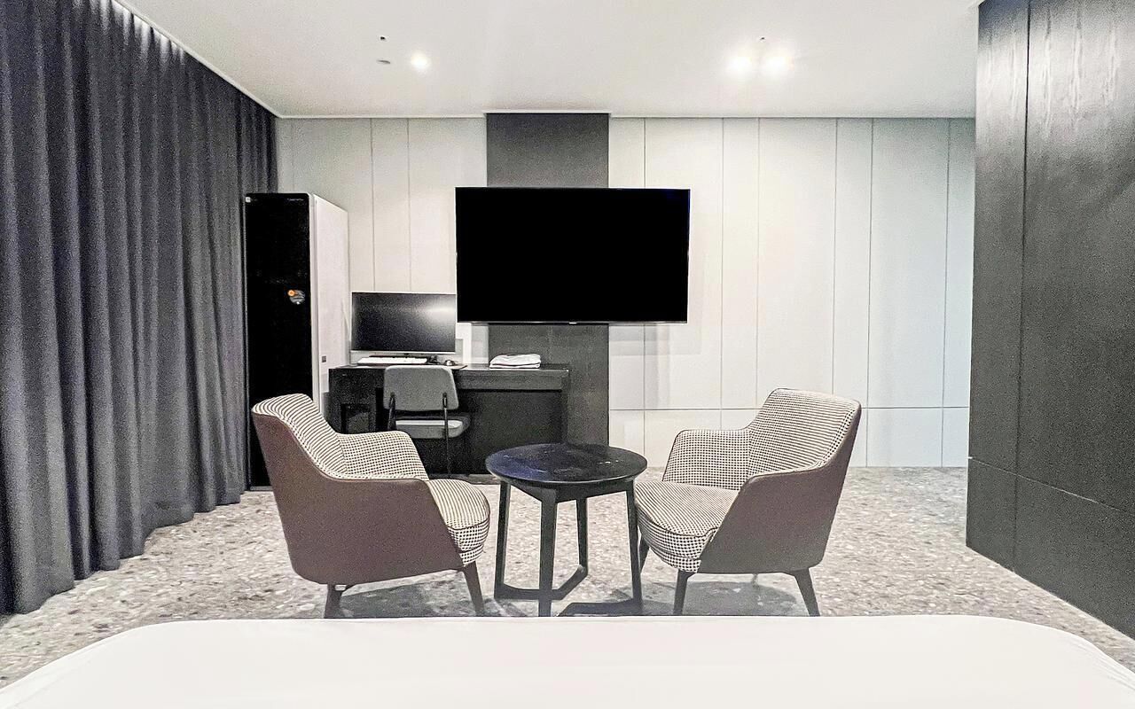 Habitación de hotel con televisor de pantalla plana en la pared, una mesita redonda, dos sillones y una cama.