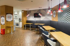 A modern restaurant interior with wooden flooring, black cushioned booths, and red pendant lighting.