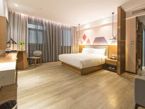 A modern hotel room with a wooden floor, a bed with white linens, a desk with a lamp, and a chair.