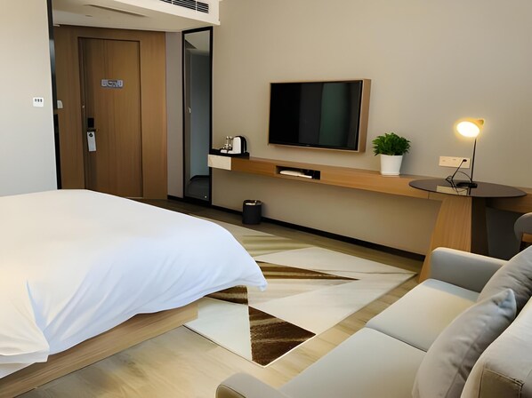 A hotel room with a bed, a sofa, a TV mounted on the wall, a small table with a plant, and a trash bin. - Borrman Hotel (Shanghai)
