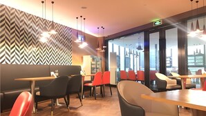 A modern restaurant interior with herringbone patterned walls, multiple seating areas, and pendant lighting.
