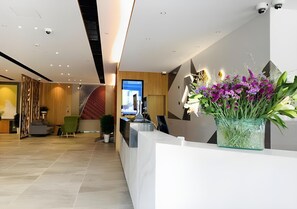 A modern reception area with a marble counter, a large floral arrangement, and a seating area with a green chair.