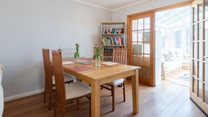 Een eethoek met een houten tafel en stoelen, een boekenkast en een glazen deur naar buiten.