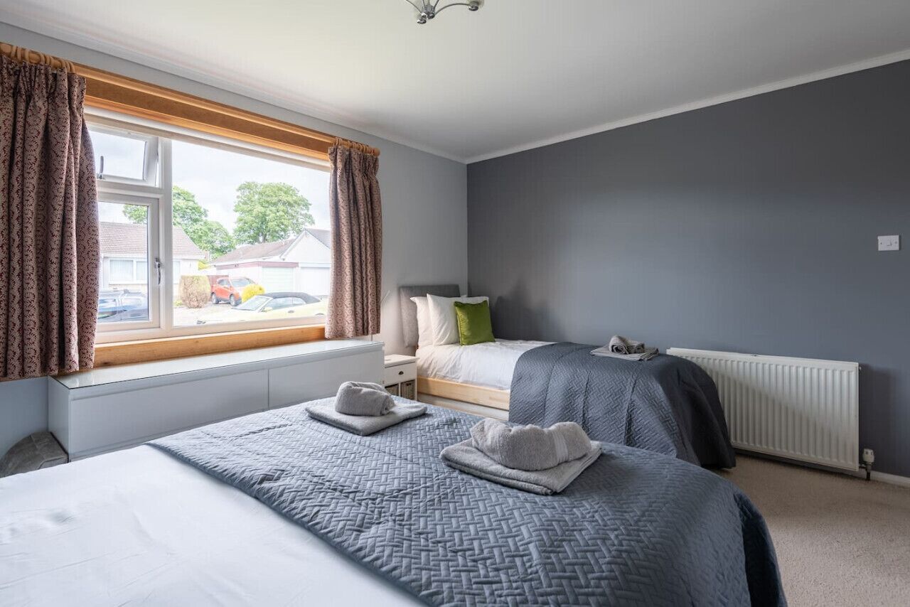 Une chambre avec deux lits, une fenêtre avec des rideaux, un radiateur et une vue sur l’extérieur.
