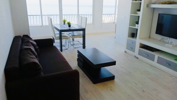 A modern living room with a sofa, a dining table with chairs, and a TV stand.