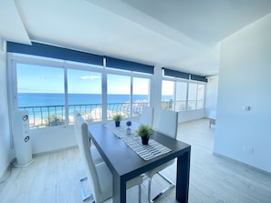 A spacious balcony with a view of the sea, a dining area with a table and chairs, and a modern interior design.